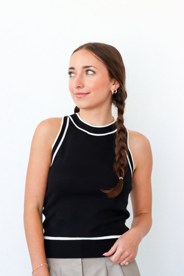 Woman wearing a black sleeveless top with white trim against a white background