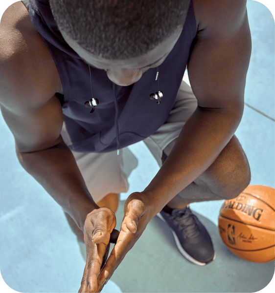 Athlete wearing headphones uses Micro Rounds | RAD wellness device on hands during basketball practice for recovery and body care outdoors.