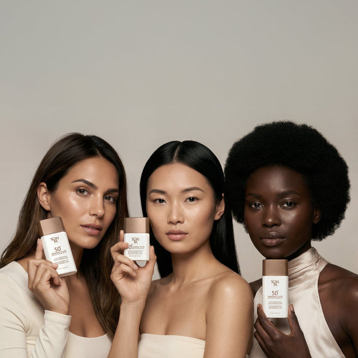 Three diverse women holding SPF 50+ Mineral Fluid | YON-KA PARIS skincare bottles, showcasing radiant skin and promoting sun protection and wellness.