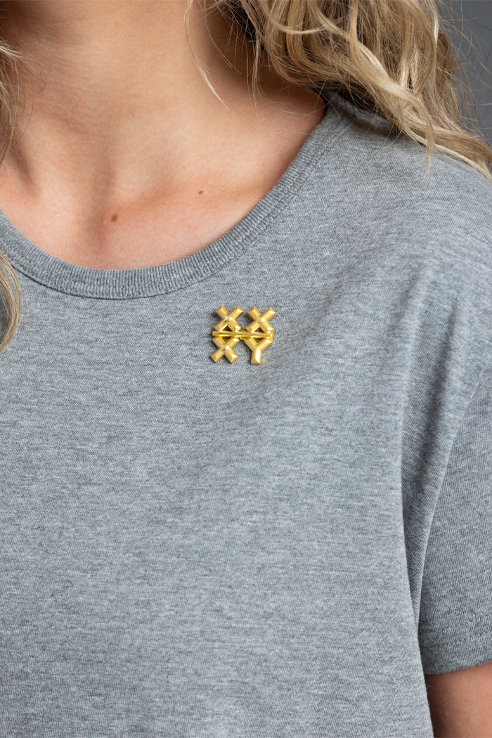 Person wearing a gray t-shirt with a gold XXXY pin || Gold