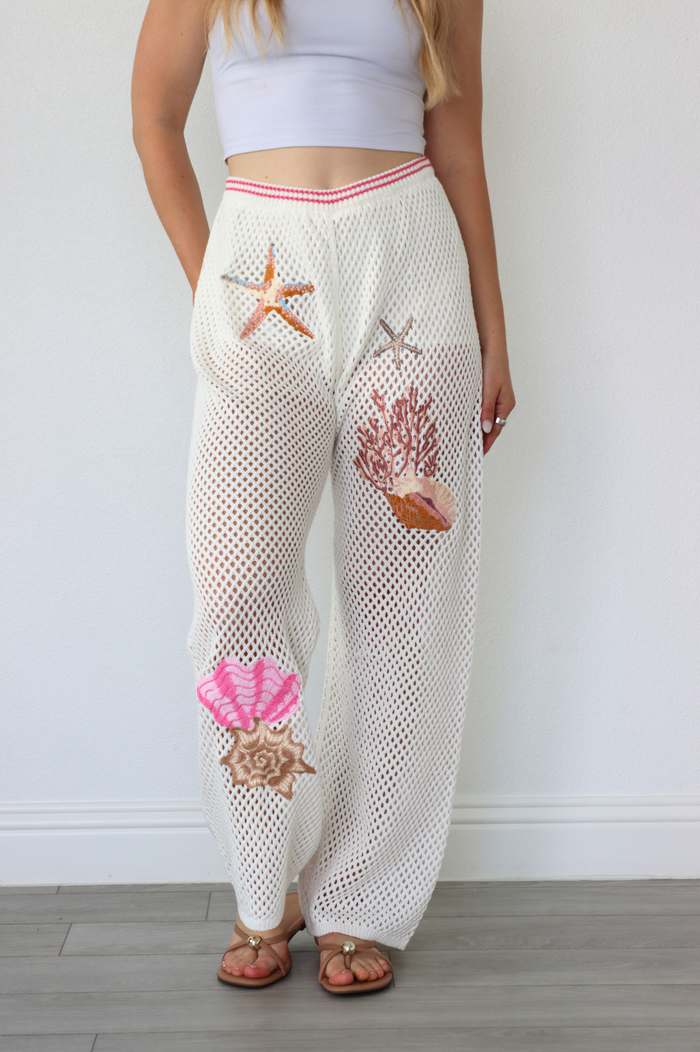 Person wearing white mesh pants with starfish and shell designs against a plain background