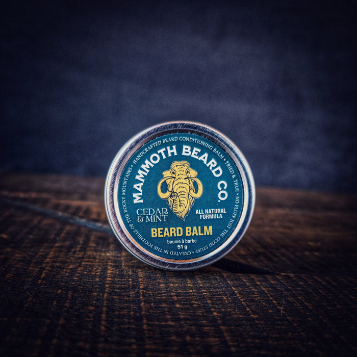 Closed tin of Cedar & Mint Beard Balm by Mammoth Beard Co on dark wood surface, natural beard conditioner with woods, mint and vanilla scent.
