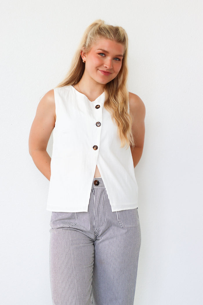 Woman wearing a white sleeveless top with buttons and striped pants against a white background