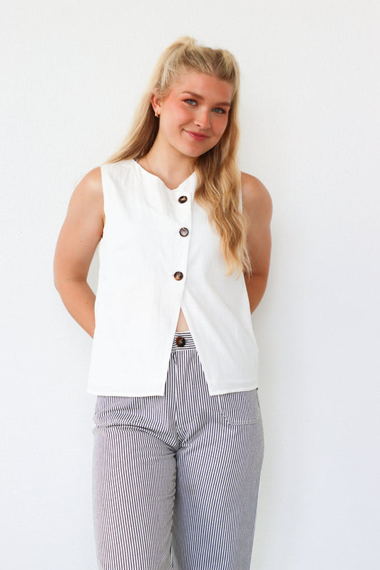 Woman wearing a white sleeveless top with buttons and striped pants against a white background