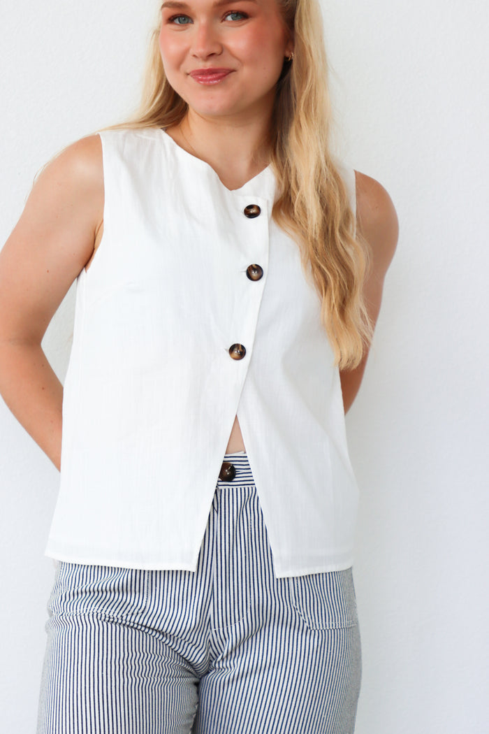 Woman wearing a white sleeveless button-up top with a plain background