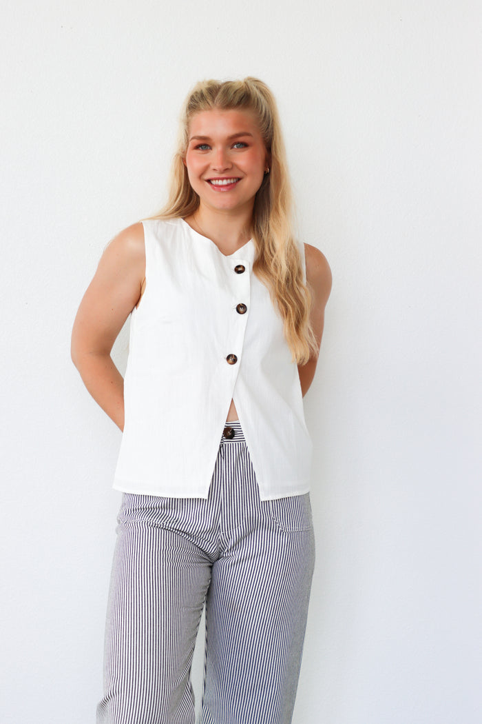Woman wearing a white sleeveless top with buttons and striped pants on a white background