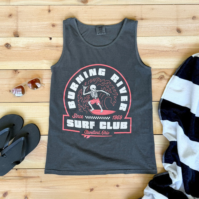 Gray tank top with 'Burning River Surf Club' graphic on a wooden surface with sunglasses and a striped towel.