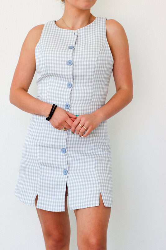 Person wearing a blue and white checkered dress with buttons on a plain background