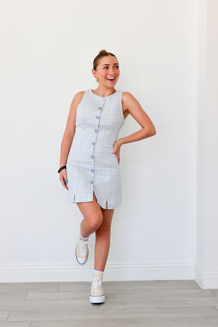 Woman wearing a sleeveless dress with buttons against a white wall
