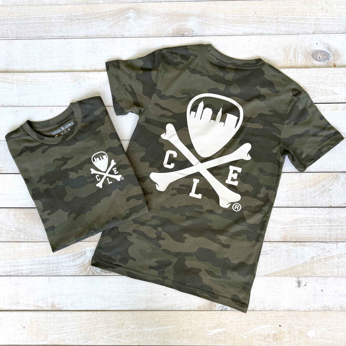 Two camouflage t-shirts with a white logo on a wooden surface