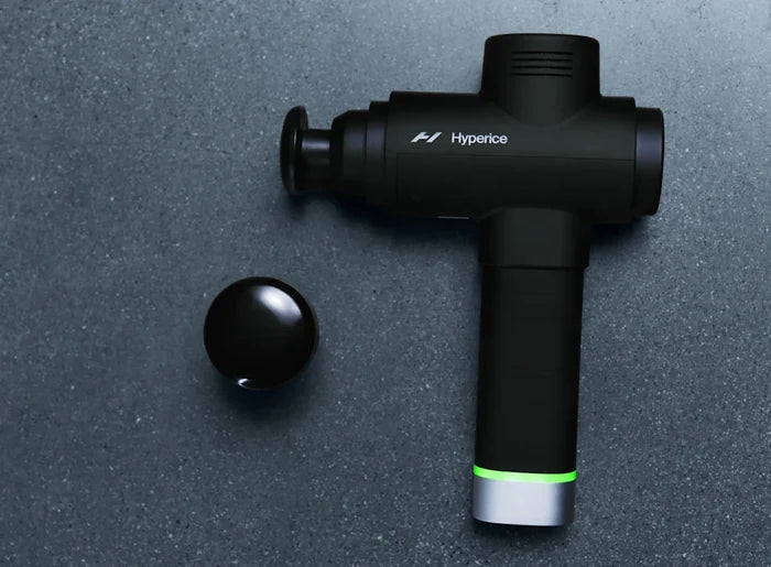 Heated Head Attachment | Hyperice shown with a black percussion massage device on a dark surface, highlighting wellness recovery tools for muscle relaxation.
