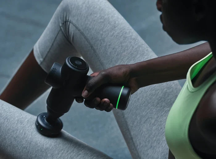 Person wearing athletic clothing using a handheld massage device with the Heated Head Attachment | Hyperice on their thigh for muscle recovery and wellness.