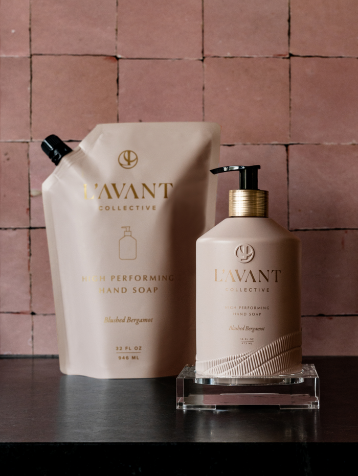 High Performing Hand Soap Refills | L'AVANT Collective showing blush beige refill pouch and matching pump bottle on dark surface with textured pink tile background, skincare hand care.