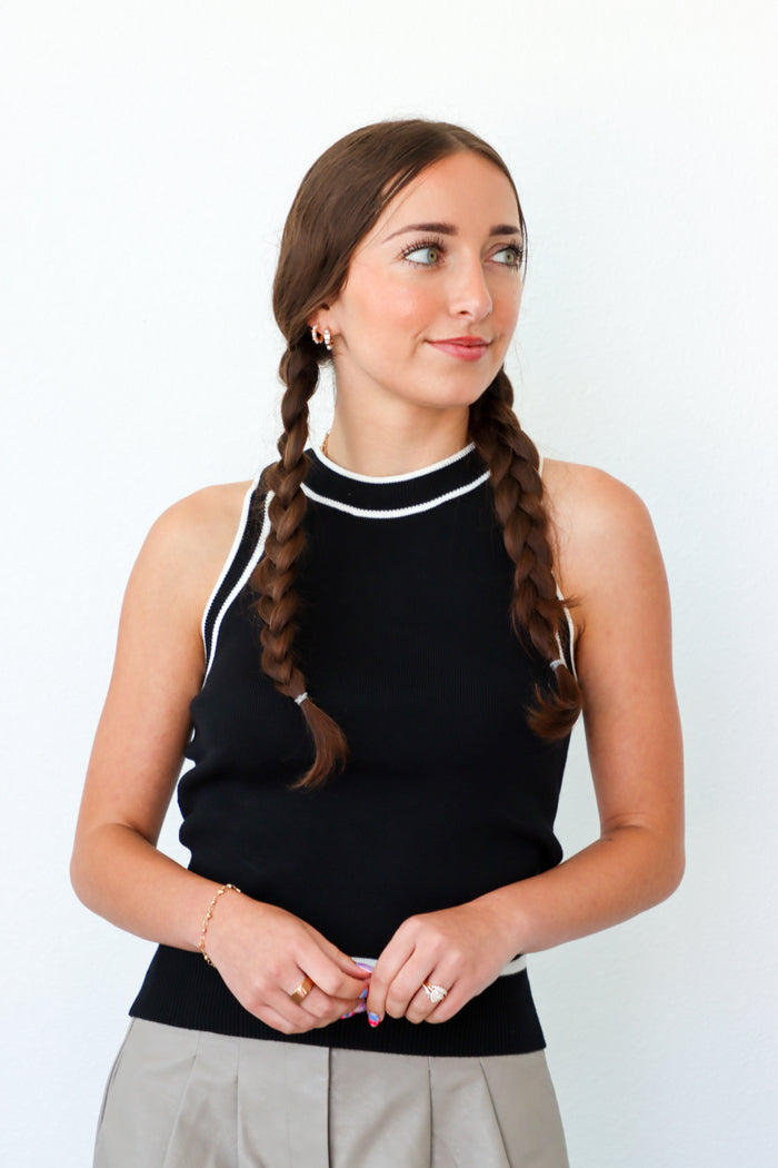 Woman wearing a black sleeveless top with white trim against a white background