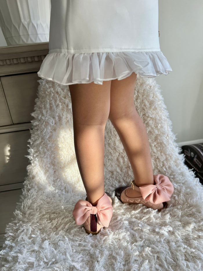 Back view of blush quilted Mary Jane shoes highlighting oversized pink bow heel detail and classic black patent cap toe.