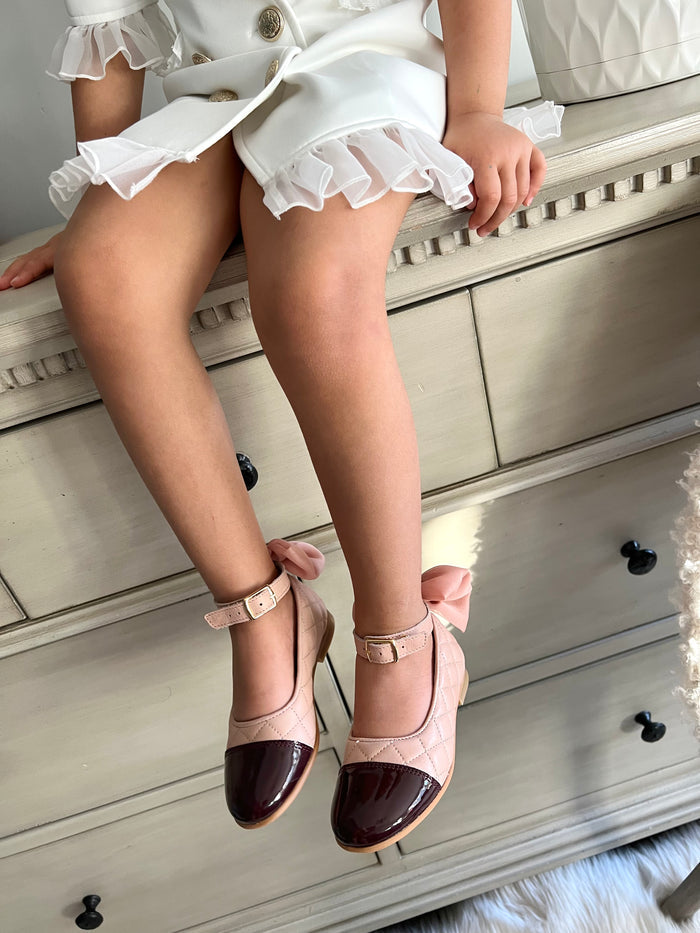 Little girl wearing blush quilted Mary Jane shoes with patent toe and bow heel, elegant girls dress shoes for special occasions.