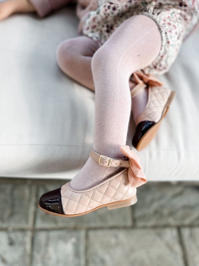 Side profile of blush quilted Mary Jane shoes with ankle strap, gold buckle closure, and structured dusty pink bow accent.
