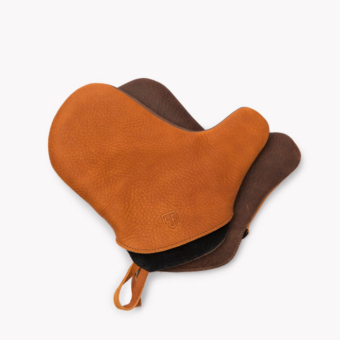 Tan and dark brown Field leather oven mitts overlapping, stamped shield logo and hanging loop visible