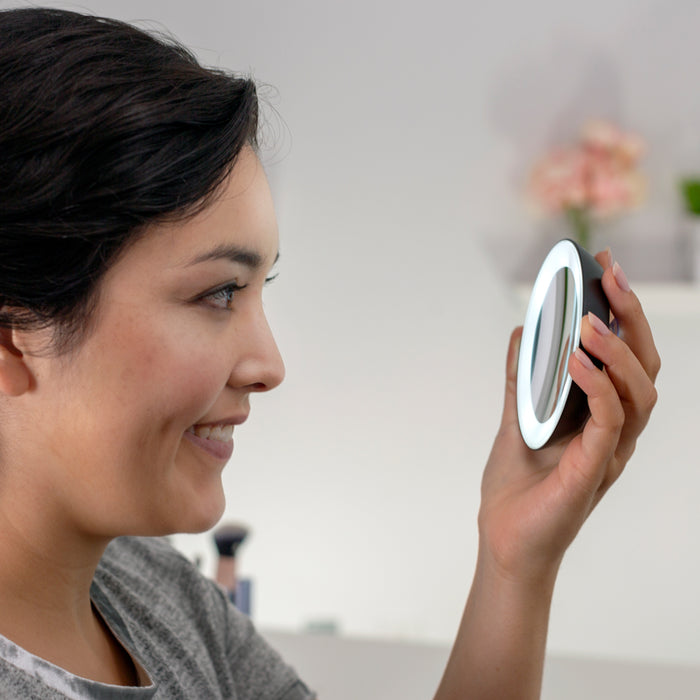 Zadro LED15X 705004419499 environment photo side view user holding lighted compact, lighted compact mirror with magnification & suction cups in front of a real life setting