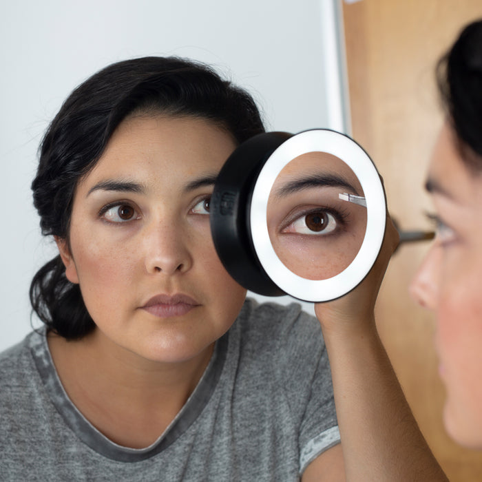 Zadro LED15X 705004419499 environment photo front view mounted on vanity mirror user tweezing eyebrows , lighted compact mirror with magnification & suction cups in front of a real life setting