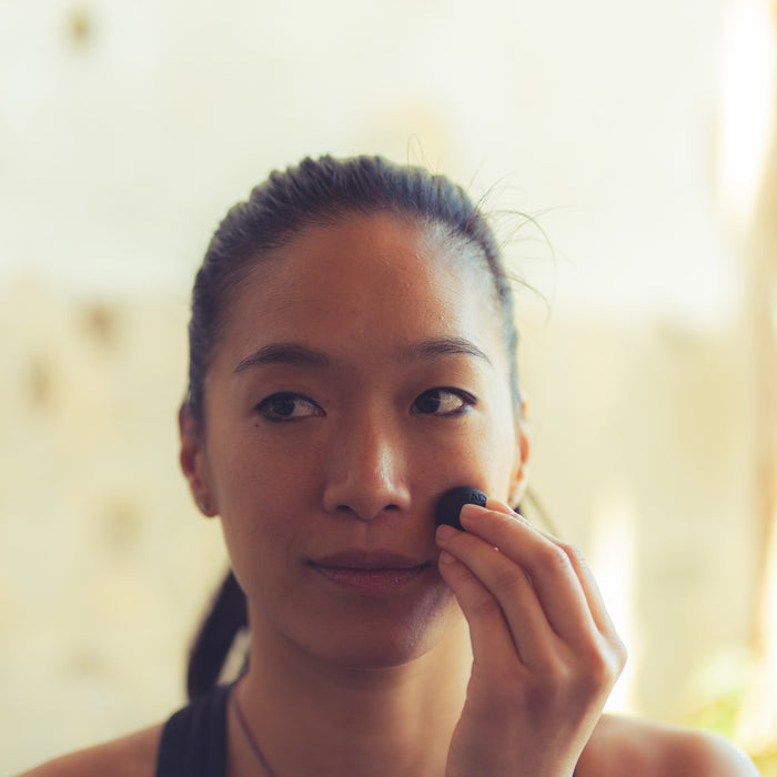 Woman applying skincare with a Micro Rounds | RAD facial tool on her cheek in a softly lit room, promoting wellness and self-care.