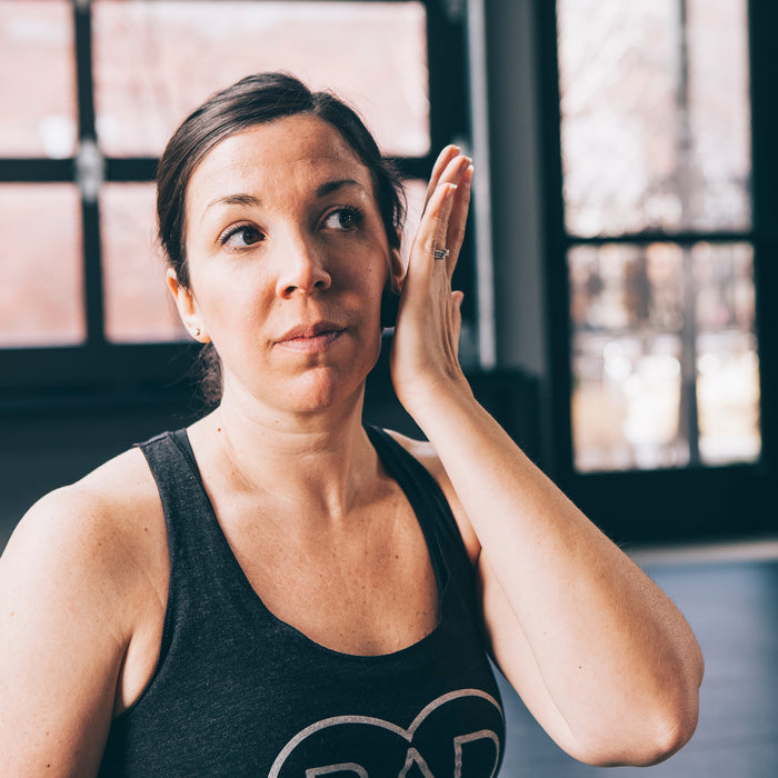 Woman in workout attire gently touching her face, demonstrating skincare or recovery routine using Micro Rounds | RAD for wellness and body care.