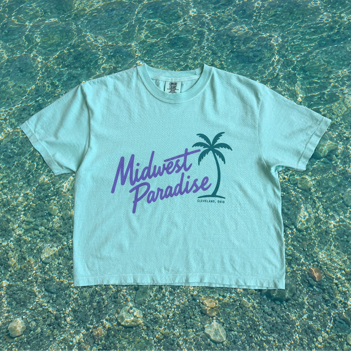 Light blue t-shirt with 'Midwest Paradise' text and palm tree graphic on a water background