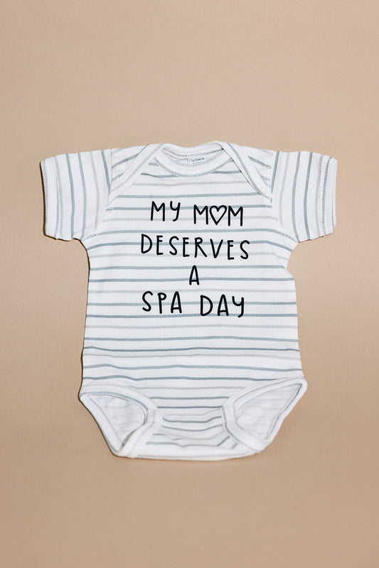 White and light gray striped baby onesie with the text "My mom deserves a spa day" printed on the front, Mom Deserves A Spa Day Baby Onesie | Lucky Owl.