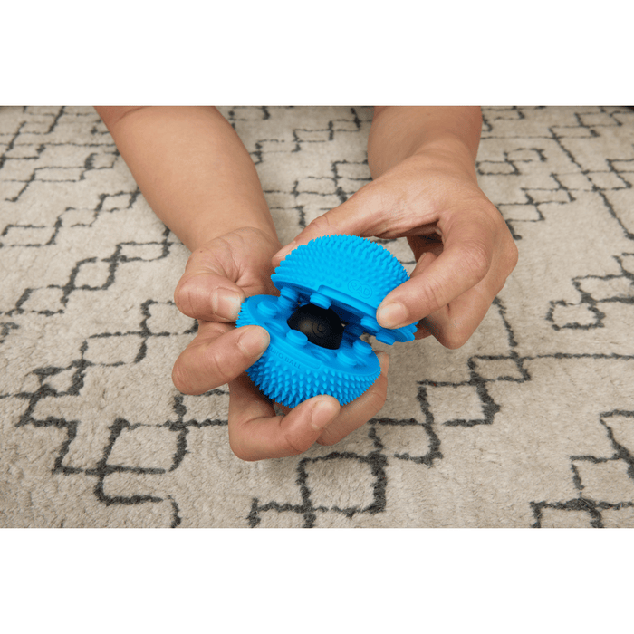 Hands holding and opening a bright blue textured Neuro Ball | RAD wellness device designed for muscle recovery and body care on a patterned carpet background.