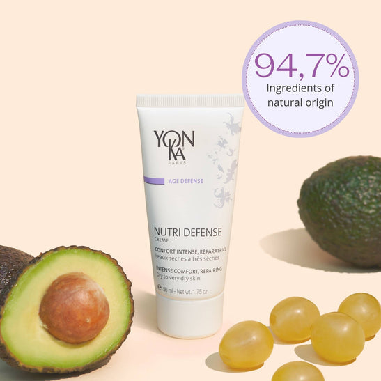 Nutri Defense Creme | Yon-Ka Paris tube standing among avocado and yellow capsules with a label showing 94.7% natural origin ingredients for skincare and intense comfort.