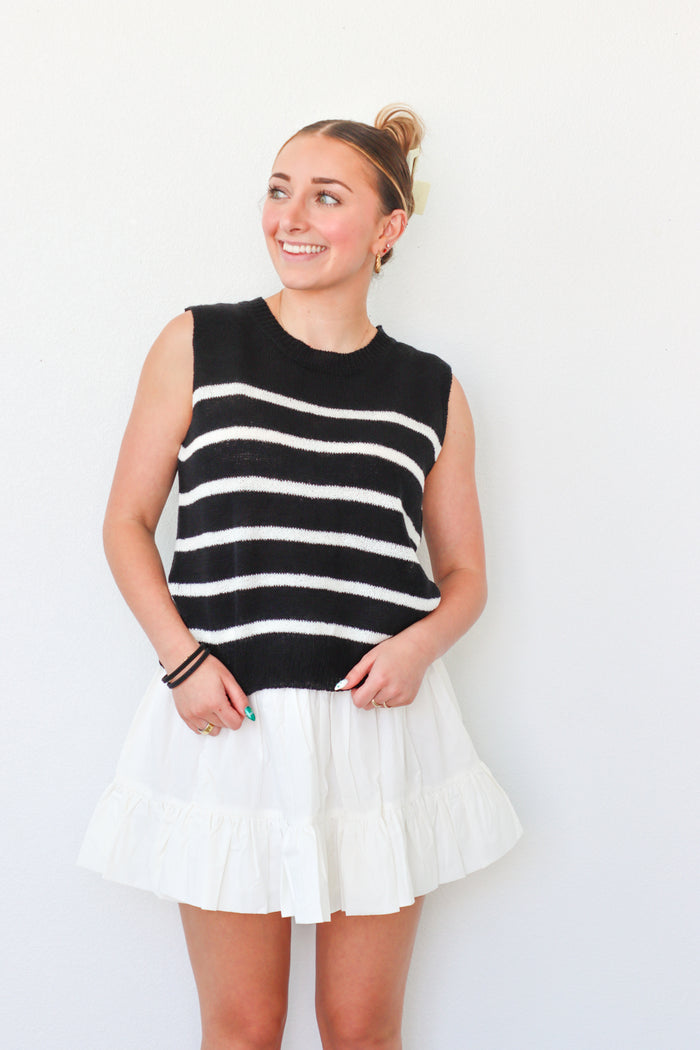 Woman wearing a black and white striped sleeveless top and white skirt against a plain background