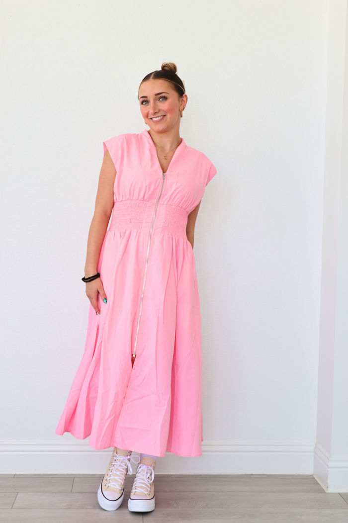 Woman wearing a pink dress standing against a white wall