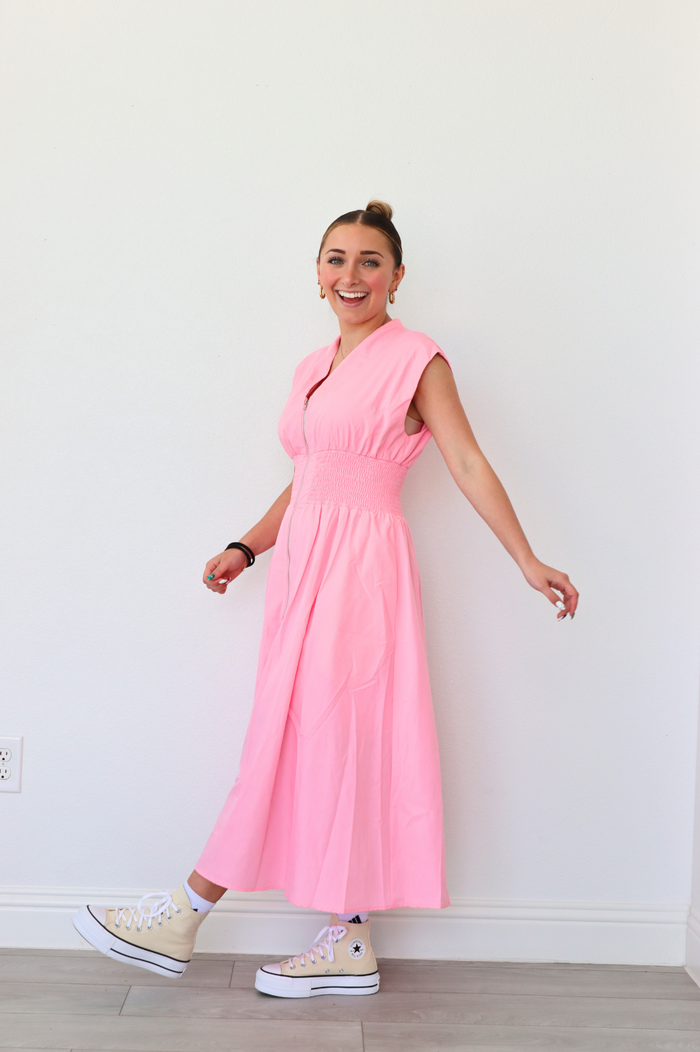 Woman wearing a pink dress standing against a white wall.
