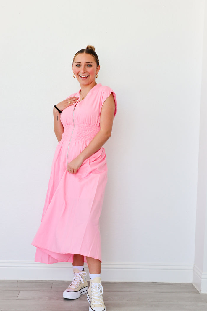 Woman wearing a pink dress standing against a white wall