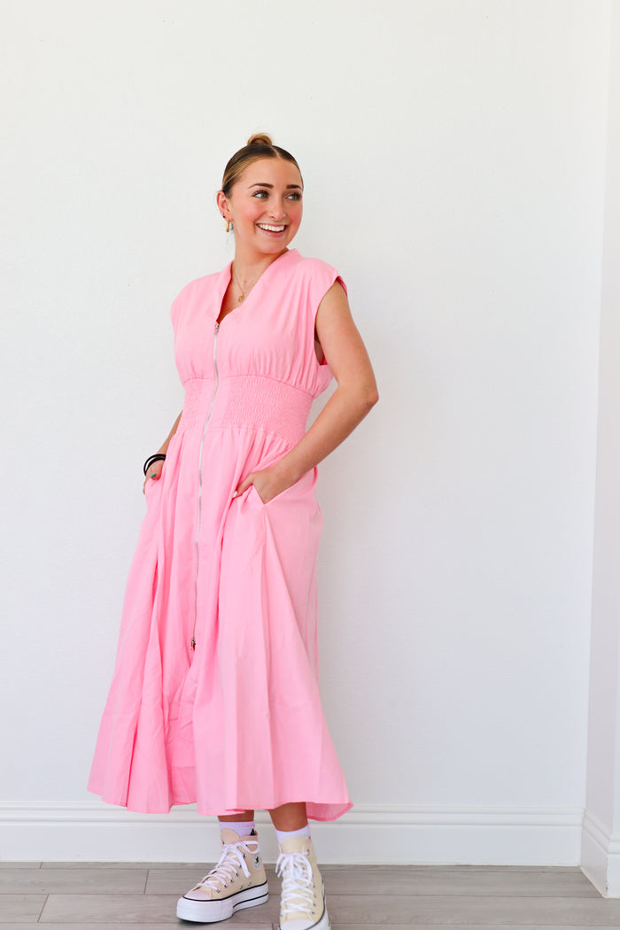 Woman wearing a pink dress standing against a white wall