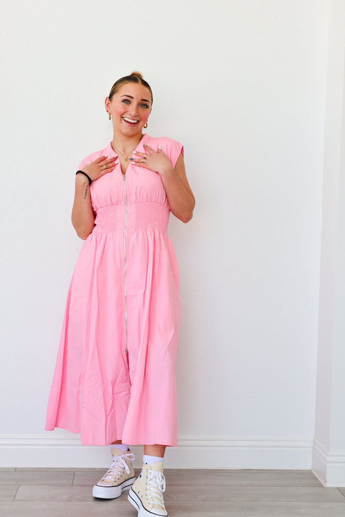 Woman wearing a pink dress standing against a white wall