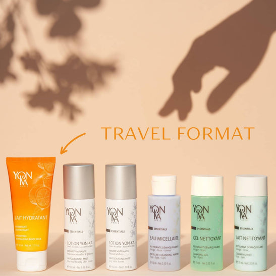 A lineup of six skincare products including lotions and cleansing gels displayed under warm light with a shadowed hand and text indicating travel size, featuring Travel Lotion Yon-Ka PNG | Yon-Ka Paris.