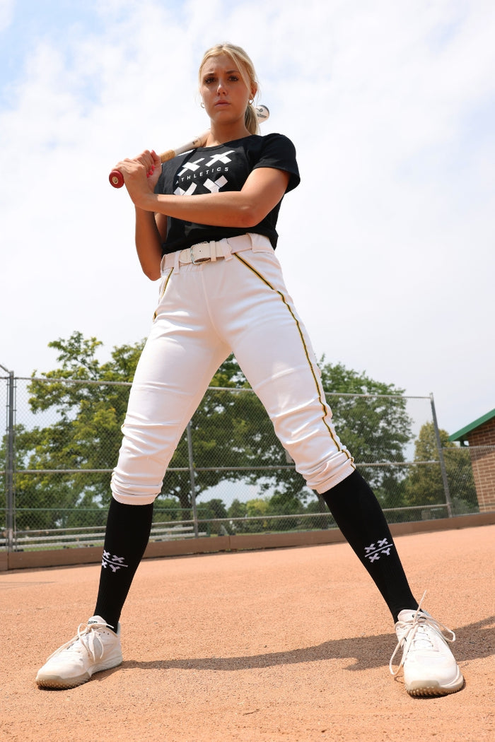 Person in softball uniform on a field with trees and sky in the background || Black